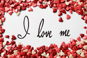 Handwritten phrase I Love Me and heart shaped sprinkles on white background, flat lay