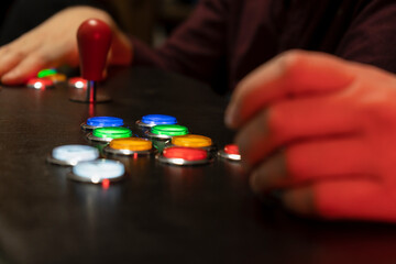 Closeup view of two people hands playing arcade vintage video games.Gamepad with joystick and many colorful buttons .Gaming concept lifestyle with creative red light.