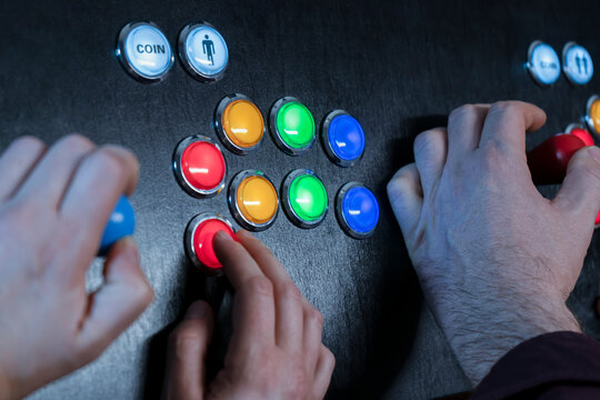 Closeup view of two people hands playing arcade vintage video games.Gamepad with joystick and many colorful buttons .Gaming concept.