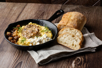 Banosh - a ukrainian dish made of cornmeal. Served in black pan with cracklings, mushrooms and hutsul cheese bryndza. Close-up isolated on a wooden background with sliced bread and grey linen napkin.