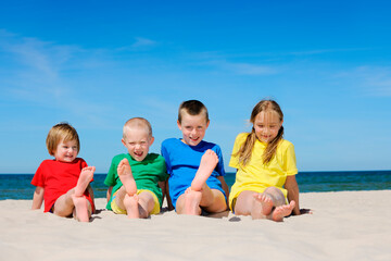 Two girls and two boys in colorful t-shirts sitting on a sandy beach