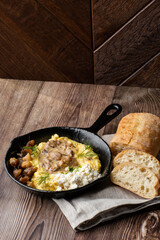 Banosh - ukrainian dish made of cornmeal. Served in black pan with cracklings, mushrooms and hutsul cheese. Close-up isolated on wooden background with sliced bread and grey linen napkin. Copy space.