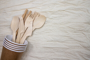Disposable bamboo cutlery in disposable paper cups on canvas background.