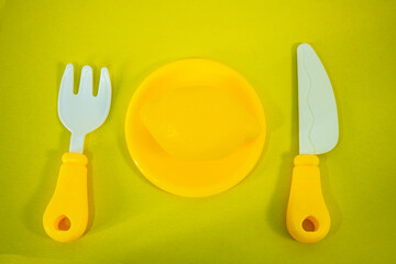 Children's fork with a knife and a plate with an artificial lemon on a bright yellow background