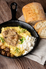 Banosh - a ukrainian dish made of cornmeal. Served in black pan with cracklings, mushrooms and hutsul cheese bryndza. Close-up isolated on a wooden background with sliced bread and grey linen napkin.