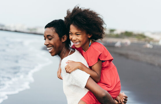 Black mother and daughter running on the beach during summer vacation - Family african people having fun together outdoor - Travel and happiness lifestyle - Soft focus on kid face