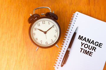 MANAGE YOUR TIME concept of alarm clock and notebook over wooden background with light leak in the morning.