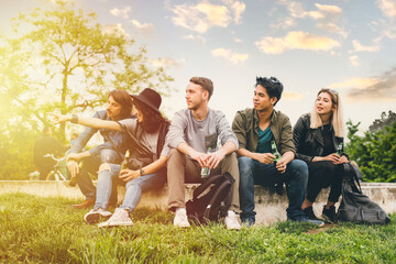 Group of multiethnic friends outdoor in the city sitting on the grass in a park looking away