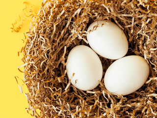 Easter white eggs in nest on yellow trend color background. Easter minimal creative composition with copy space. Spring Happy Easter holiday. Top view.