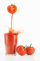 Tomato juice pouring into glass on white