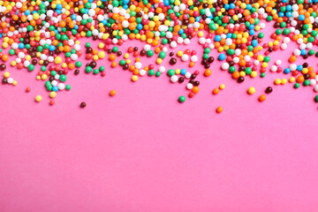 Bright colorful sprinkles on pink background, flat lay with space for text. Confectionery decor