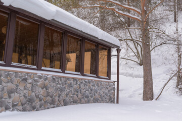Wall of a building in a mountainous area. Solid glazing, stone wall. Background - a mountain with trees and bushes, white snow. Chalet concept.
