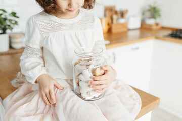 Cute young girl holding glass jar with heart shaped cookies.