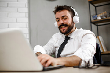 Naklejka premium Attractive businessman in office. Young businessman with headphones singing at work