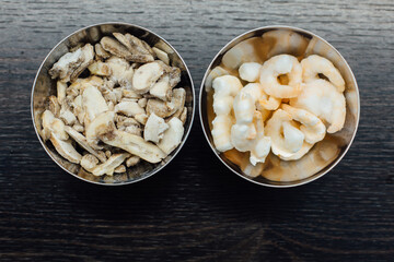 Food preparation for cooking. Frozen shrimps and frozen mushrooms in a metal bowl on a dark brown kitchen surface