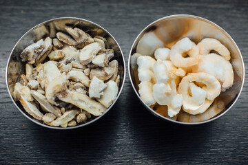 Food preparation for cooking. Frozen shrimps and frozen mushrooms in a metal bowl on a dark brown...