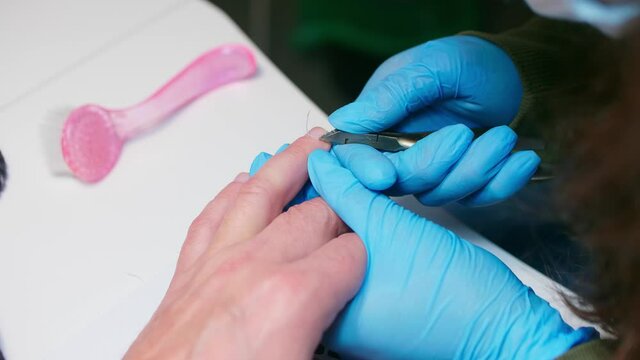 Manicurist uses metal nippers to remove dry skin of cuticle around nails. Processe of manicure.