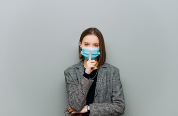 A female worker in formal clothes stands against a gray wall and touching her finger to her lips...