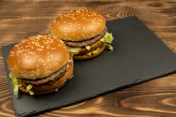 Two gourmet delicious burgers with french fries slices on a black board on a wooden background. Fast food