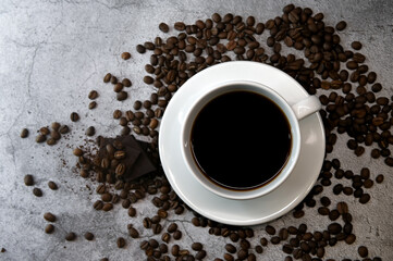Close up of a cup of coffee surrounded with coffee beans and dark chocolate. Top view