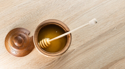 Honey with wooden honey dipper in wooden bowl on wooden table
