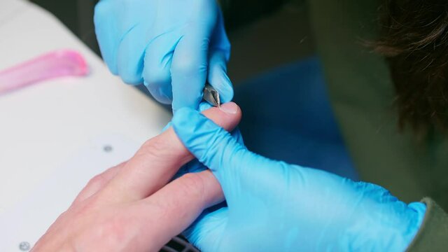 Manicurist uses metal nippers to remove dry skin of cuticle around nails. Processe of manicure.