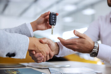 Closeup of car seller and buyer shaking hands. Car seller handing a car keys to a buyer. Car salon...