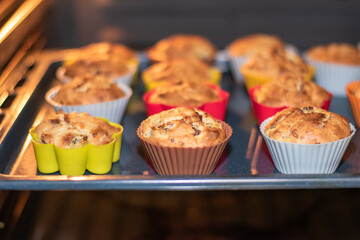 Muffins with dried fruits are baked in the oven in multi-colored silicone molds. Close-up of baked goods in the oven. Place for an inscription.
