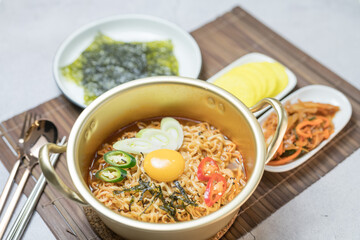 Korean traditional Ramyeon noodle  with egg yolk, chilli, kimchi in a traditional korean noodle pot, Spicy Korean Ramyeon instant noodle a traditional dish.