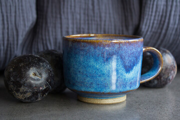 Still life with blue ceramic cup and plums on textured background. 