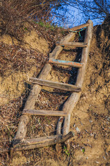 A makeshift wooden ladder made of logs lies on a dirt cliff and stretches towards the blue sky