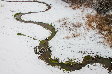 The stream winds through a snow-covered clearing, and car tires are lying on it