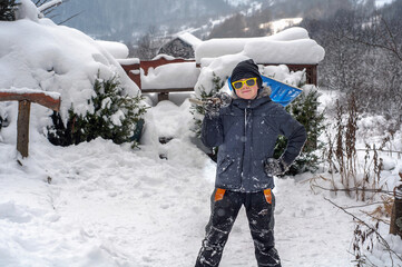 Fototapeta na wymiar Boy cleans the snow-covered paths near the house. Heavy snowfalls in winter. Changing weather conditions. Disaster. Large drifts of snow. The child helps to do the male work of cleaning the snow