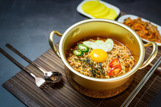 Korean style instant noodle, Ramyeon with egg yolk, chilli, kimchi vegetables pickled and radish pickles in a traditional korean noodle pot.