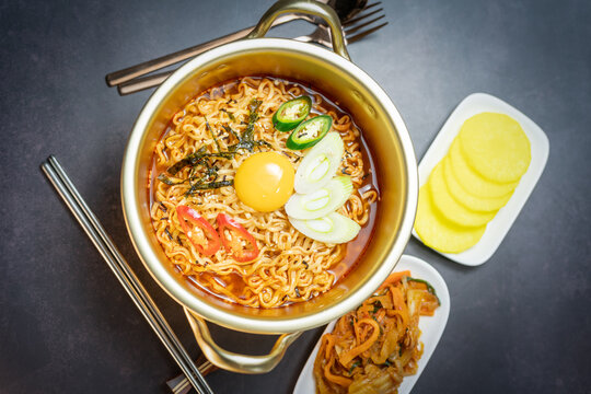 Korean style instant noodle, Ramyeon with egg yolk, chilli, kimchi vegetables pickled and radish pickles in a traditional korean noodle pot.