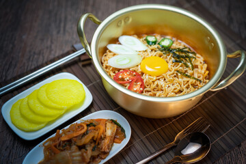 Korean style instant noodle, Ramyeon with egg yolk, chilli, kimchi vegetables pickled and radish pickles in a traditional korean noodle pot.
