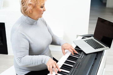 elderly woman learning to play synthesizer piano on laptop online at home