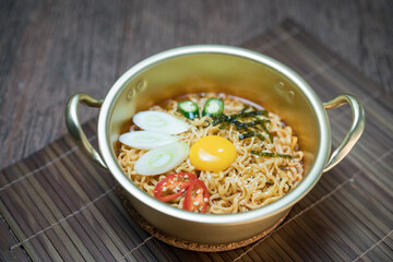 Korean style instant noodle, Ramyeon with egg yolk, chilli, kimchi vegetables pickled and radish pickles in a traditional korean noodle pot.