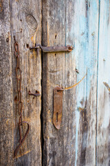 The simplest rustic door lock. A rusty padlock on a wooden door of an old rustic building. Old cracked wood planks burnt out in the sun.