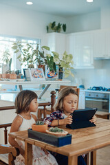 Little brother and sister playing a game or reading some story on a tablet at tablet in modern living room.