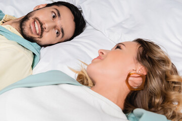 Obraz na płótnie Canvas Muslim man smiling at girlfriend on blurred foreground on hotel bed