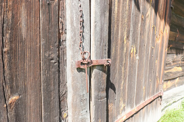 The simplest rustic door lock. A rusty padlock on a wooden door of an old rustic building. Old cracked wood planks burnt out in the sun.