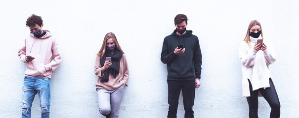 Naklejka premium Friends using mobiles covered with mask during Covid-19 out brake - Multiracial people using smart phone with face masks - New normal during pandemic - New normal lifestyle concept - Blue Filter