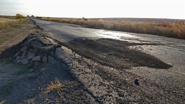 Damaged road. Dangerous road. Asphalt was made of poor materials and poor quality. Mobile photo.