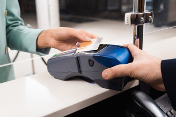 Cropped view of hotel receptionist with payment terminal and woman with credit card in hotel lobby