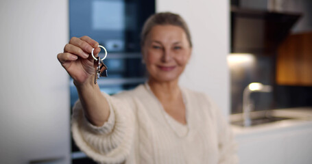 Portrait of smiling senior woman showing keys to new house at camera