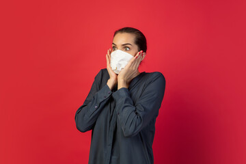 Shocked, scared. Woman in protective face mask isolated on red studio background. New rules of COVID spreading prevention. Copyspace for ad. Pandemic, healthcare and medicine, coronavirus concept.