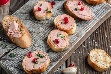 Meat liver pate on toasted bread with fruit seeds and spice herb on a wood cutting board. Top view.