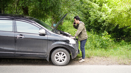 Asian man opened the hood of the car while calling