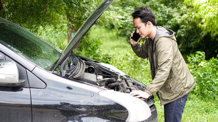 Asian man opened the hood of the car while calling